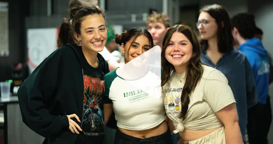 Three students posing together for a photo indoors, smiling.